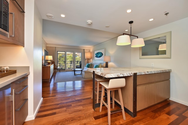 kitchen featuring a kitchen bar, kitchen peninsula, hanging light fixtures, and dark wood-type flooring