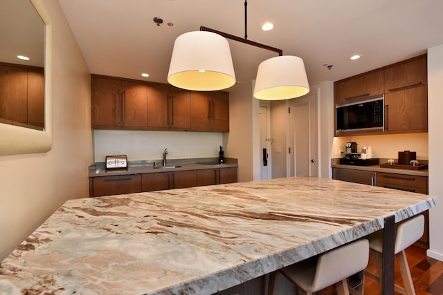 kitchen featuring stainless steel microwave, dark wood-type flooring, decorative light fixtures, and sink