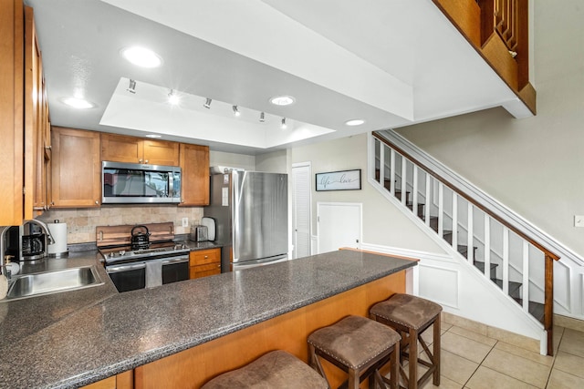 kitchen with a raised ceiling, kitchen peninsula, sink, and appliances with stainless steel finishes