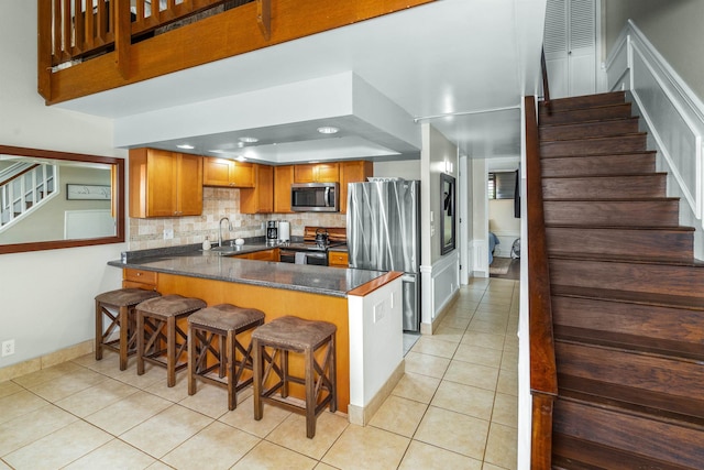 kitchen featuring kitchen peninsula, stainless steel appliances, light tile flooring, backsplash, and a kitchen bar