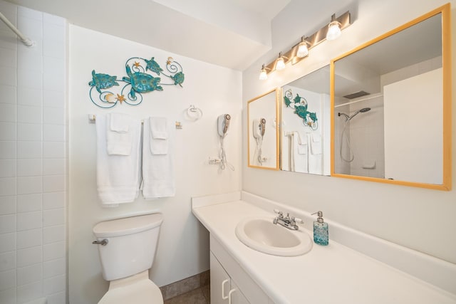 bathroom with tiled shower, vanity, and toilet