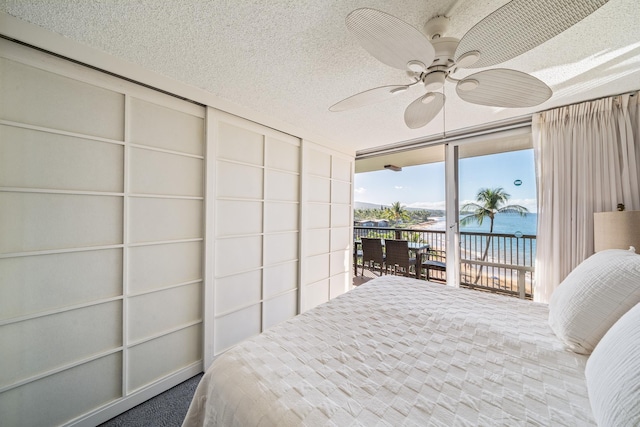 bedroom with access to outside, a textured ceiling, a water view, and ceiling fan