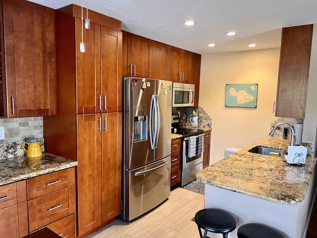 kitchen featuring decorative backsplash, light stone counters, stainless steel appliances, a kitchen bar, and a sink