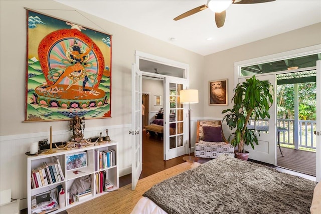 bedroom featuring wood finished floors, a ceiling fan, french doors, wainscoting, and access to outside