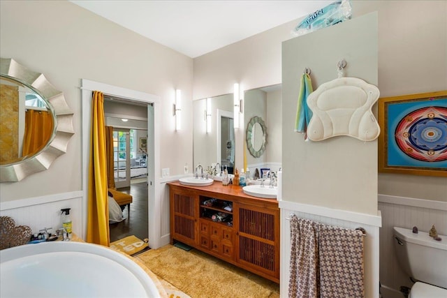 full bath with toilet, a wainscoted wall, double vanity, and a sink