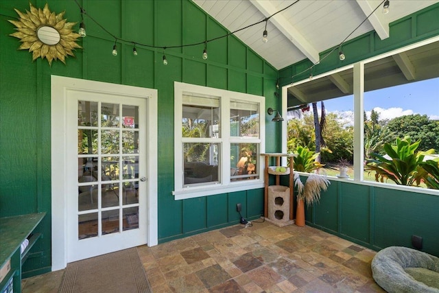 sunroom featuring beam ceiling, high vaulted ceiling, and stone tile flooring