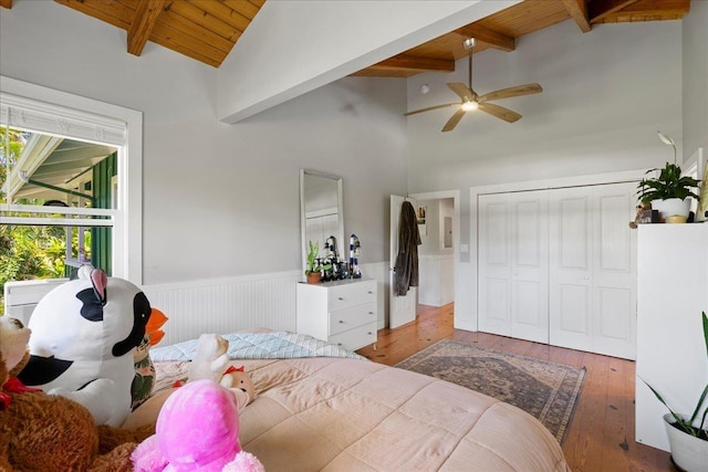 bedroom with a closet, wainscoting, wood-type flooring, wood ceiling, and beamed ceiling