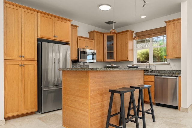 kitchen featuring a kitchen island, appliances with stainless steel finishes, a breakfast bar, sink, and dark stone counters