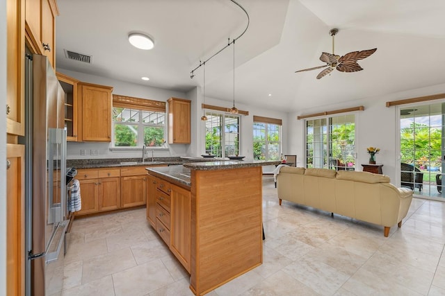 kitchen featuring sink, a breakfast bar area, high end fridge, a kitchen island, and dark stone counters