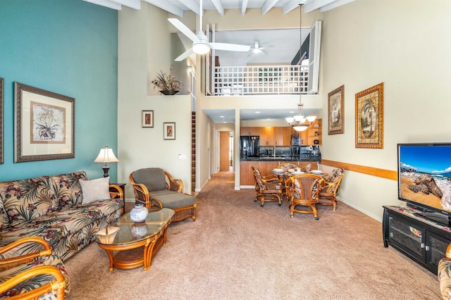 living room featuring ceiling fan with notable chandelier, beamed ceiling, light colored carpet, and a high ceiling