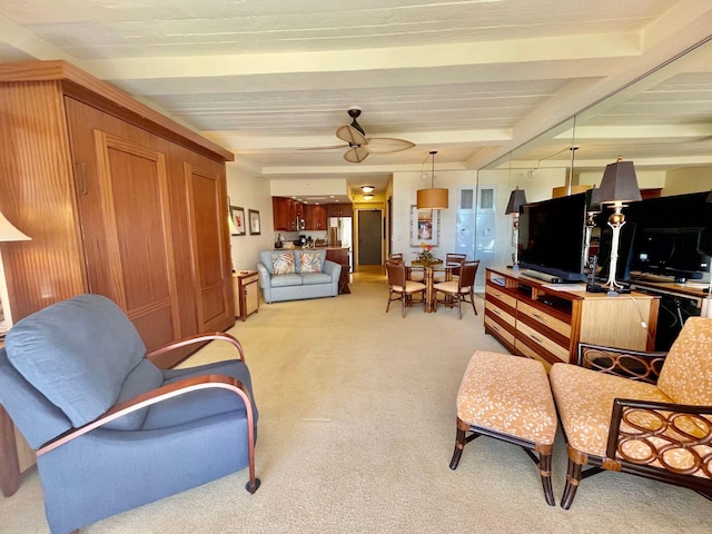 sitting room featuring light colored carpet, beamed ceiling, and ceiling fan