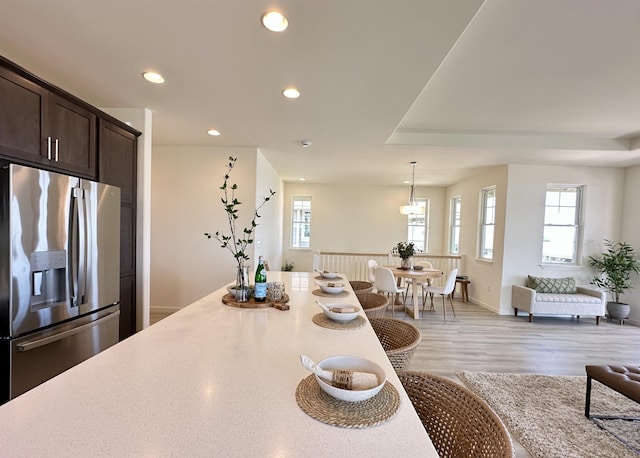 kitchen with stainless steel refrigerator with ice dispenser, recessed lighting, light countertops, open floor plan, and dark brown cabinetry