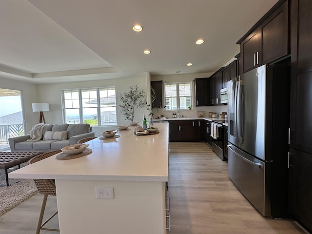 kitchen with a kitchen island, open floor plan, appliances with stainless steel finishes, light wood finished floors, and a kitchen bar