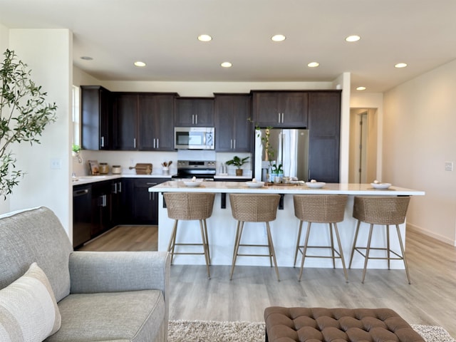 kitchen with stainless steel appliances, light countertops, light wood-style flooring, open floor plan, and a kitchen bar