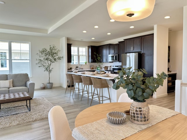 kitchen with dark brown cabinetry, recessed lighting, stainless steel appliances, a kitchen breakfast bar, and light wood finished floors