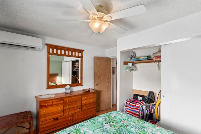 bedroom with a textured ceiling, a wall mounted air conditioner, a closet, and ceiling fan