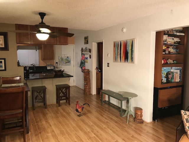 kitchen with a textured ceiling, kitchen peninsula, a kitchen breakfast bar, ceiling fan, and light hardwood / wood-style floors