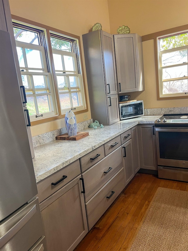 kitchen with hardwood / wood-style floors, plenty of natural light, light stone counters, and stainless steel appliances