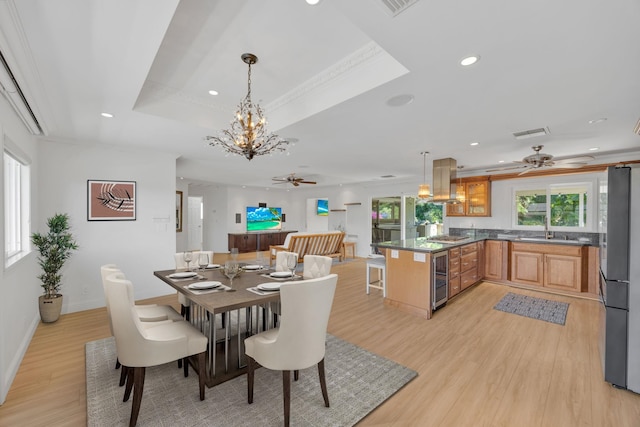 dining area with a raised ceiling, crown molding, light hardwood / wood-style flooring, and beverage cooler