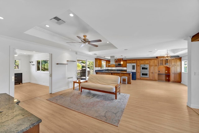 living room featuring ceiling fan with notable chandelier, light hardwood / wood-style floors, a raised ceiling, and crown molding