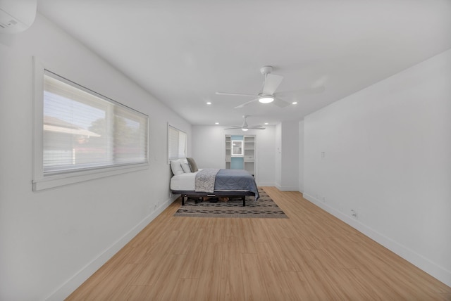 bedroom featuring a wall mounted air conditioner, light hardwood / wood-style flooring, and ceiling fan