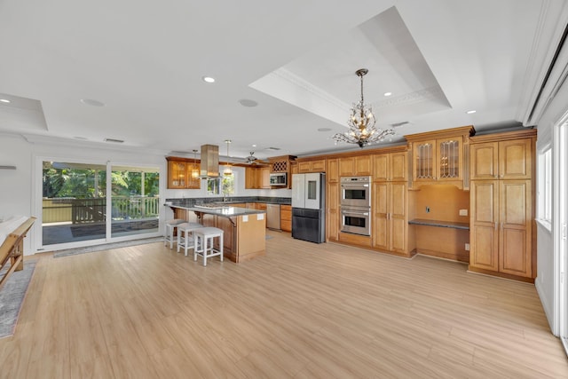 kitchen with a center island, crown molding, appliances with stainless steel finishes, a tray ceiling, and a kitchen bar