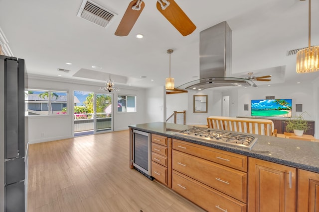 kitchen with a raised ceiling, hanging light fixtures, island exhaust hood, beverage cooler, and stainless steel appliances