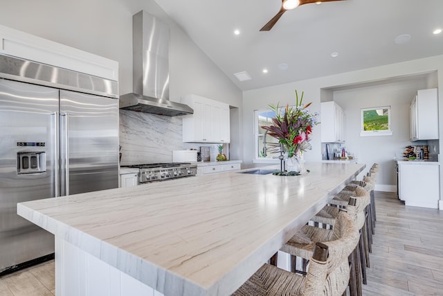 kitchen featuring white cabinetry, wall chimney exhaust hood, stainless steel appliances, light hardwood / wood-style floors, and vaulted ceiling