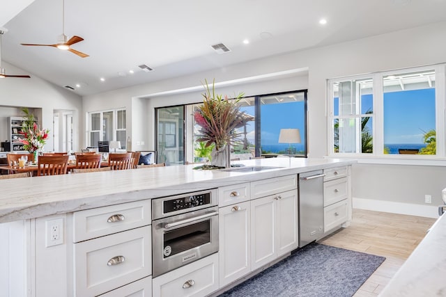 kitchen featuring light stone counters, ceiling fan, light hardwood / wood-style floors, white cabinetry, and lofted ceiling