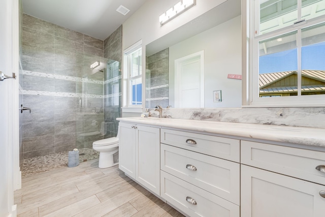 bathroom featuring hardwood / wood-style floors, vanity, toilet, and a tile shower