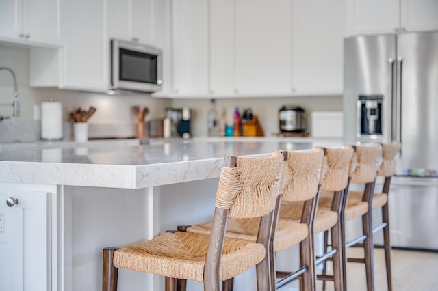 kitchen featuring a breakfast bar, stainless steel fridge, and white cabinetry