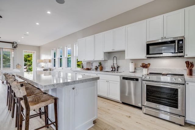 kitchen featuring stainless steel appliances, sink, a center island, light hardwood / wood-style floors, and white cabinetry