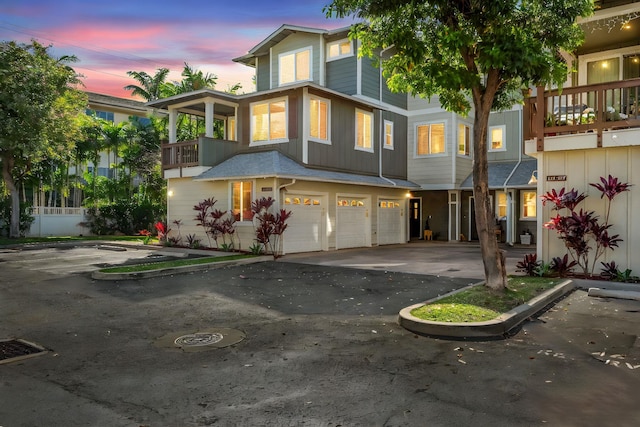 view of front of home featuring an attached garage, a balcony, aphalt driveway, and board and batten siding