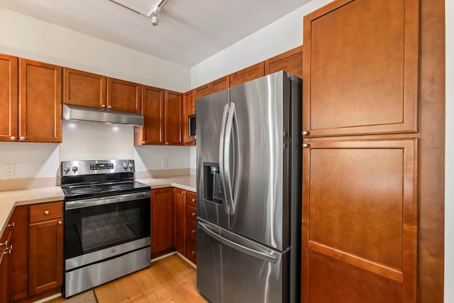 kitchen with light countertops, light wood-style flooring, appliances with stainless steel finishes, brown cabinetry, and under cabinet range hood