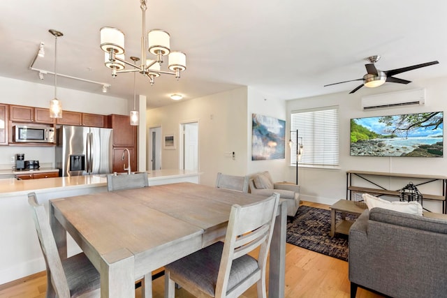 dining area featuring light wood finished floors, baseboards, ceiling fan with notable chandelier, and a wall mounted AC