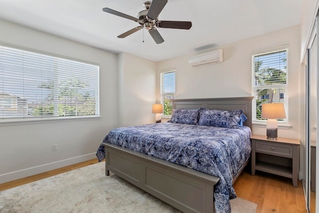 bedroom with ceiling fan, light wood-style flooring, baseboards, and a wall mounted AC