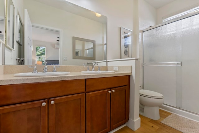 bathroom with a stall shower, double vanity, a sink, and wood finished floors