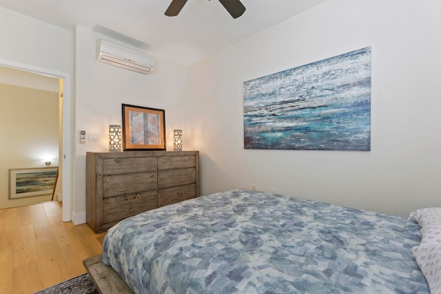 bedroom with light wood-style floors, an AC wall unit, and ceiling fan