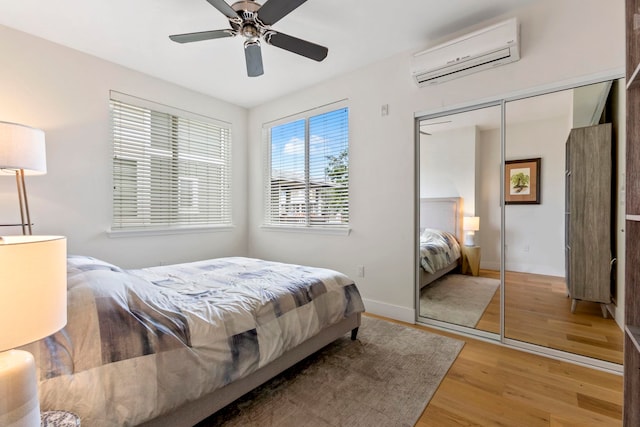 bedroom with baseboards, ceiling fan, wood finished floors, a wall mounted air conditioner, and a closet