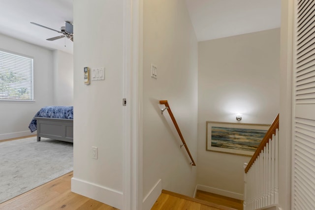 stairs featuring wood finished floors, a ceiling fan, and baseboards