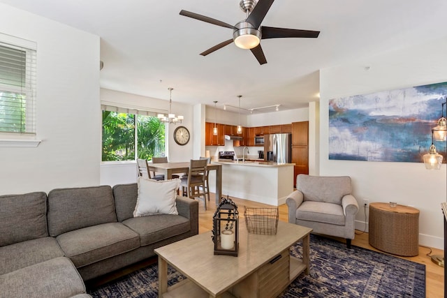 living area featuring ceiling fan with notable chandelier, rail lighting, baseboards, and wood finished floors