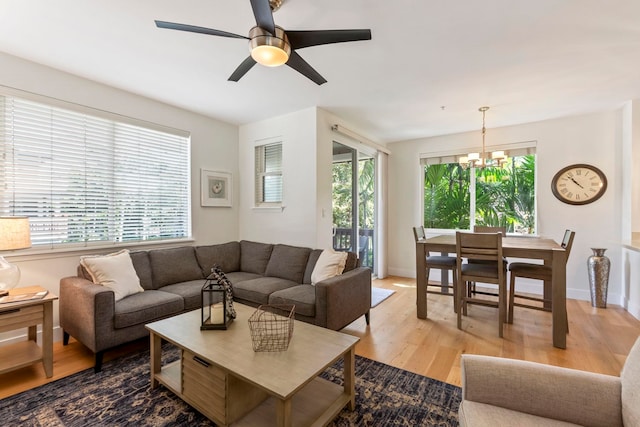 living area with a wealth of natural light, baseboards, light wood finished floors, and ceiling fan with notable chandelier