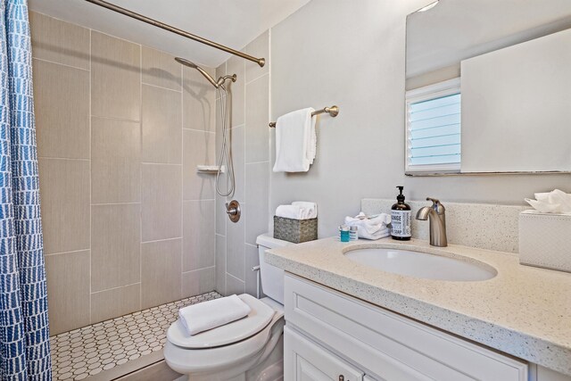 bathroom with toilet, tiled shower, and vanity