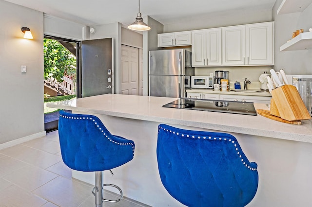 kitchen featuring a peninsula, a breakfast bar, white cabinets, freestanding refrigerator, and decorative light fixtures