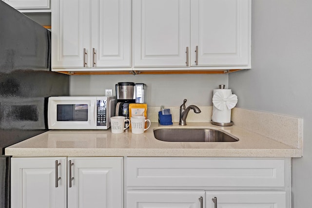 kitchen featuring white microwave, a sink, white cabinetry, and light stone countertops