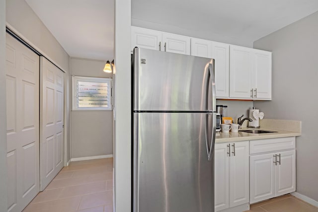 kitchen with light tile patterned floors, freestanding refrigerator, light countertops, white cabinetry, and a sink