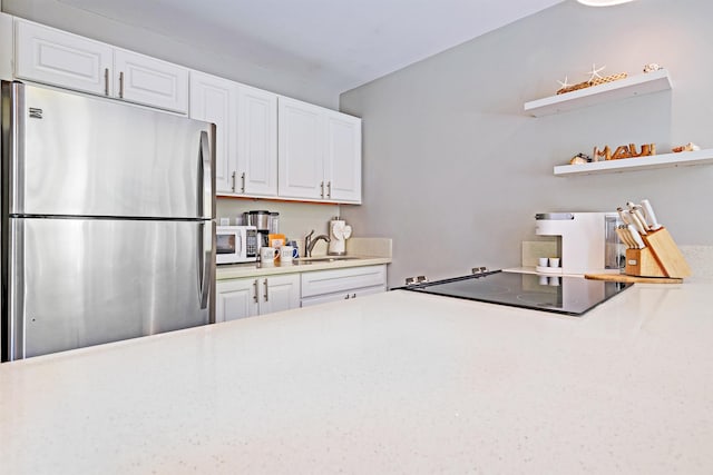 kitchen with light countertops, white microwave, freestanding refrigerator, white cabinetry, and a sink