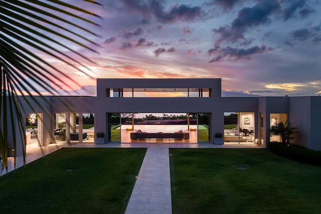 back house at dusk featuring a yard and a patio area