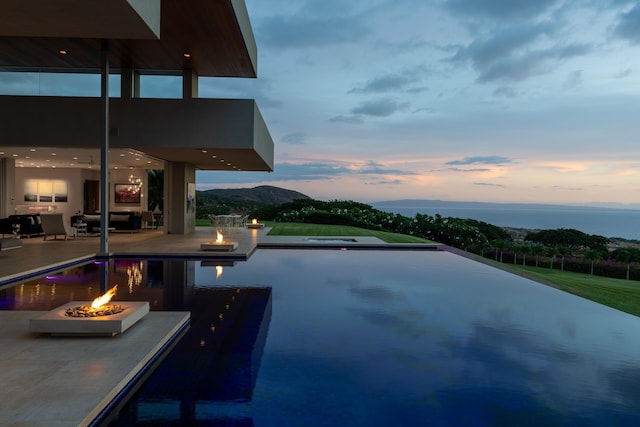 pool at dusk with a mountain view, a patio area, and an outdoor fire pit