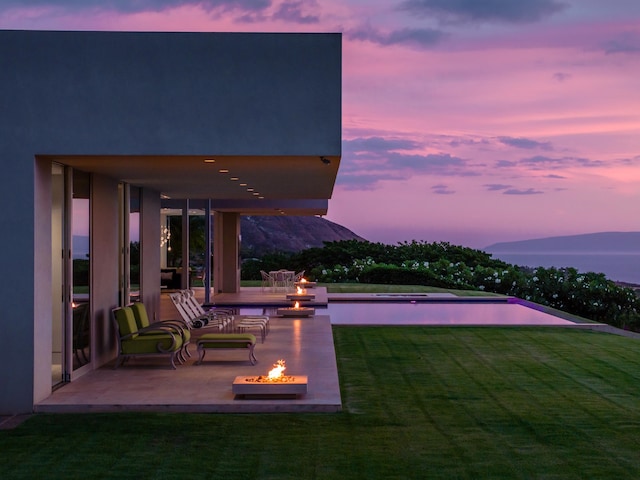 pool at dusk featuring a lawn, a mountain view, a patio area, and an outdoor fire pit